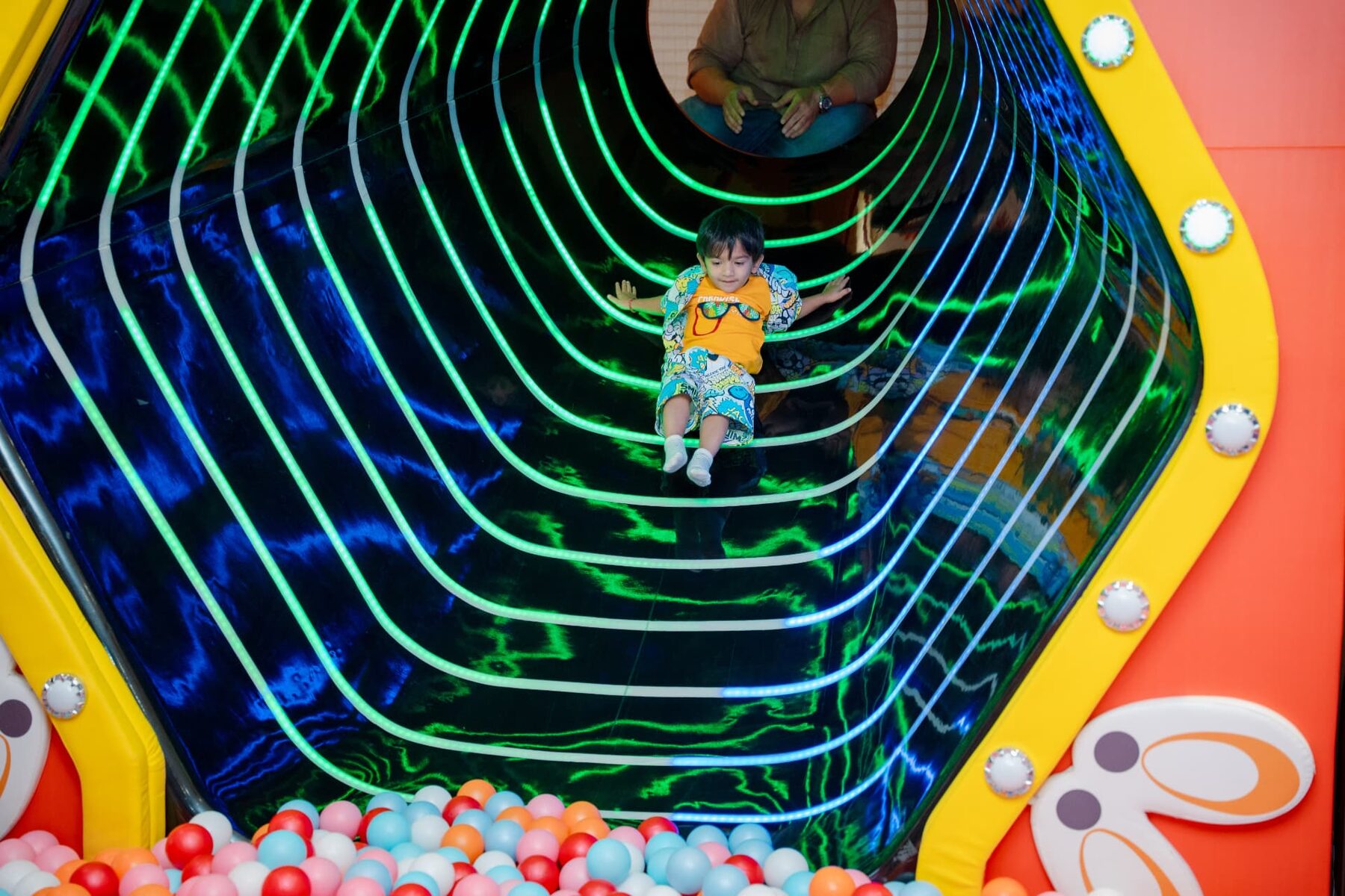 Child crawling through a glowing neon tunnel at Baccha Party Powai